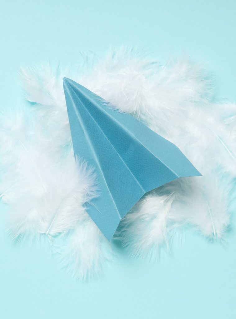 Paper plane and feathers on blue background